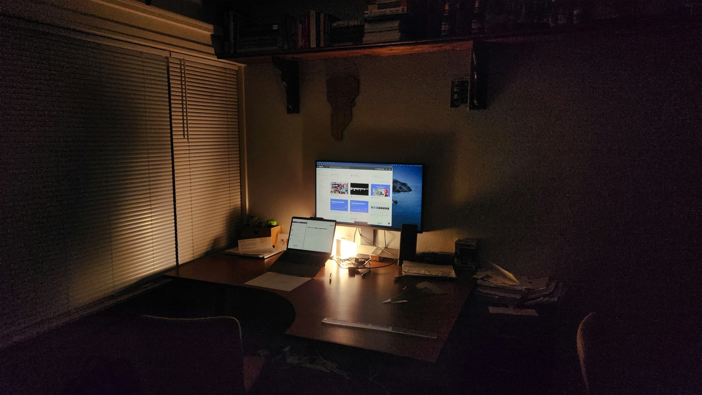 Dim night desk with laptop and monitor glow, papers and books nearby